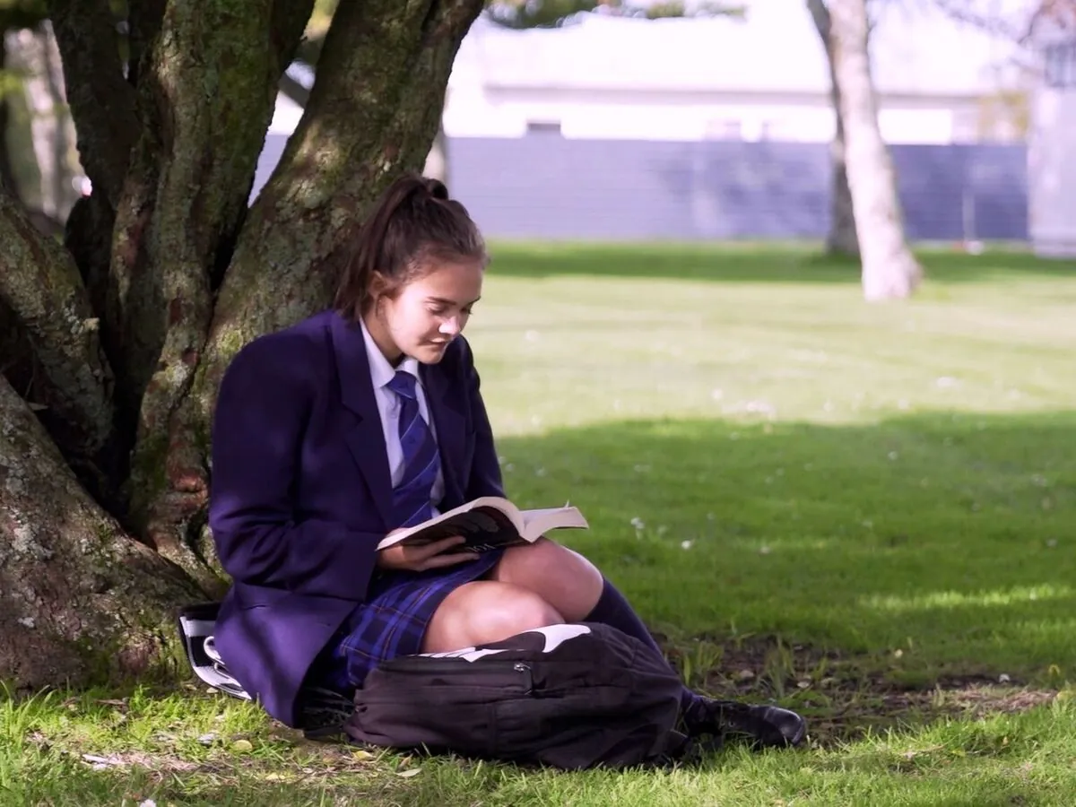 Student reading under a tree on the school grounds