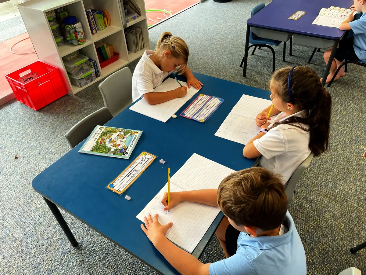 Primary students writing at a classroom table
