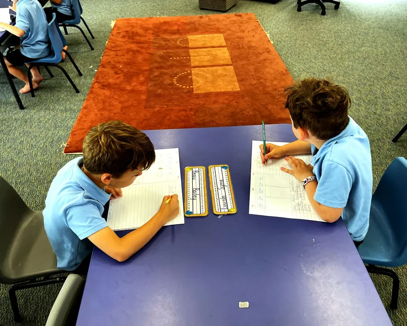 Two primary students writing at a classroom table