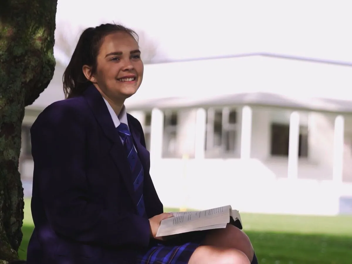 Student smiling while sitting under a tree on campus